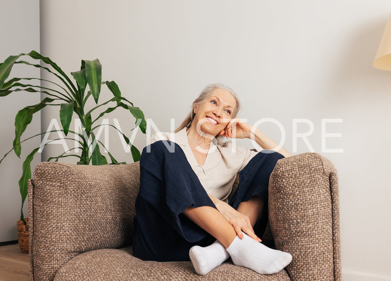 Cheerful senior woman relaxing in an armchair at home. Smiling aged female in casuals in living room.