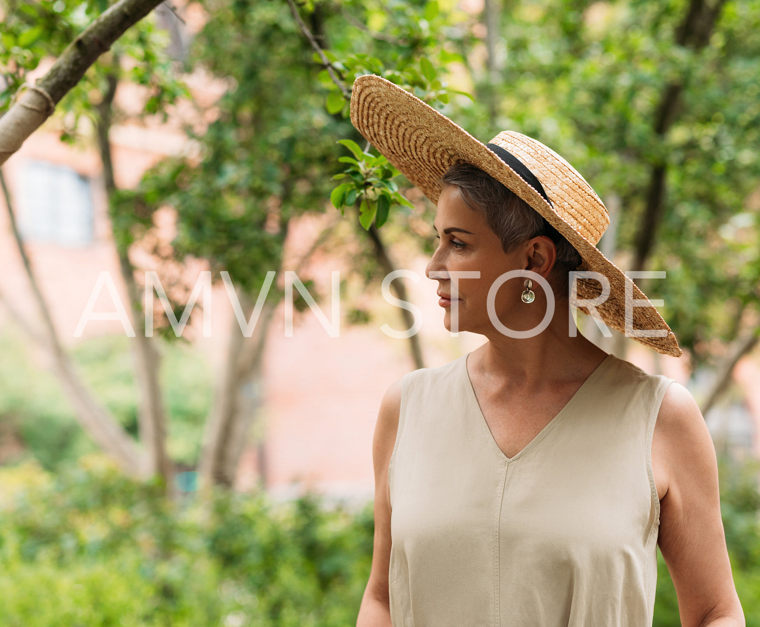 Mature woman with short hair wearing a straw hat standing in a park 