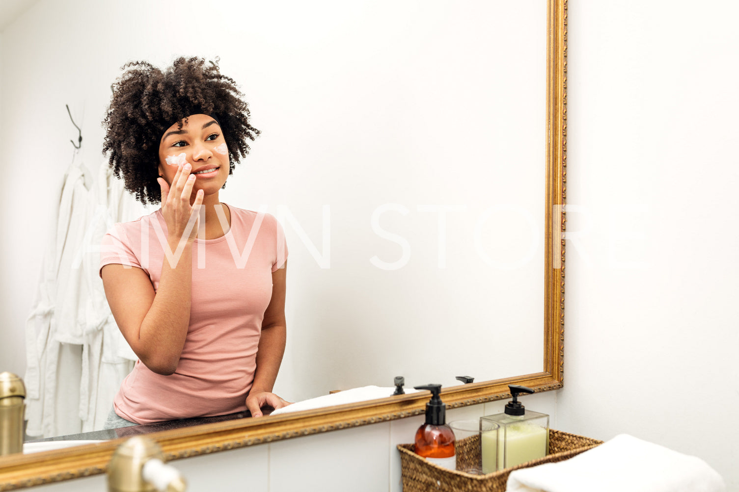 Young woman putting cosmetic cream on her face and looking into a mirror	