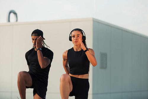 Two athletes doing warming-up exercises on a roof at sunset. Man and woman doing high-intensity exercises together.