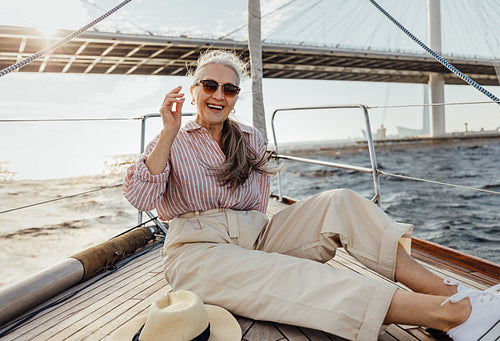 Happy mature woman resting on a yacht bow. Smiling female enjoying boat trip wearing sunglasses.