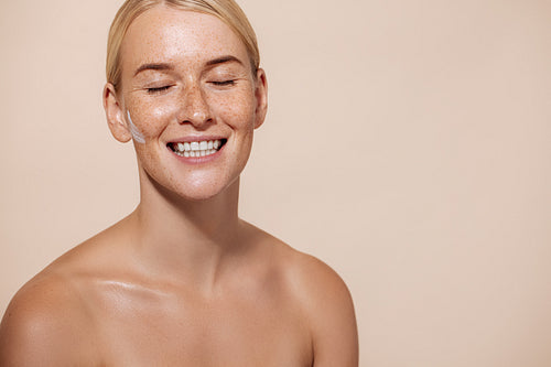 Studio portrait of young happy woman with facial cream on cheek