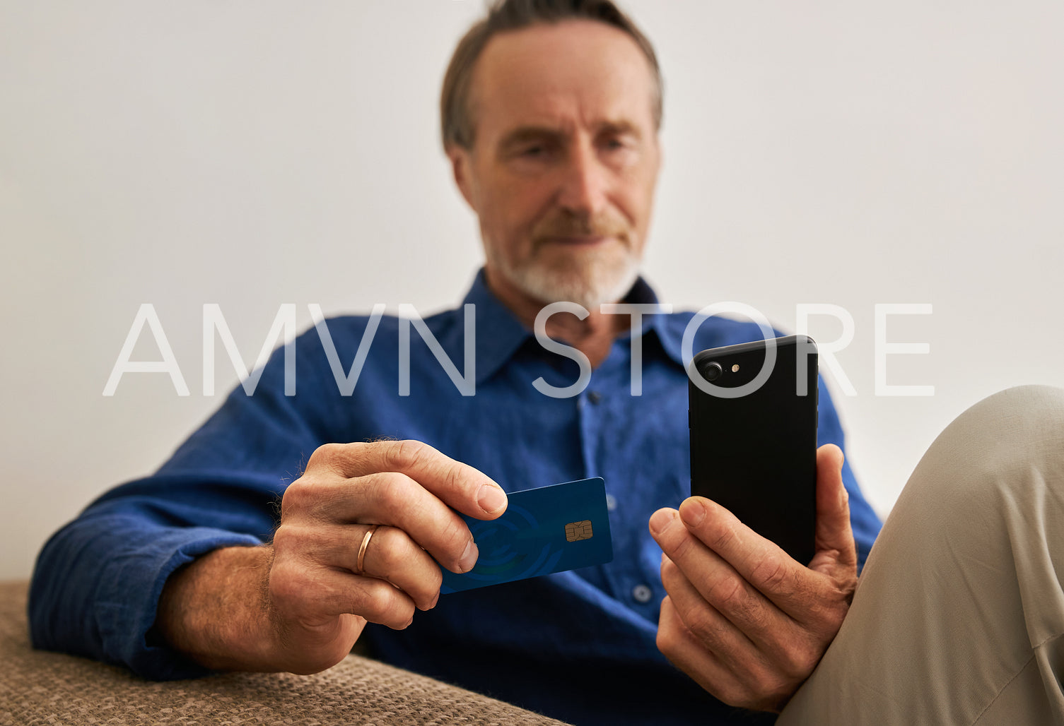 Close up of hands of a senior man holding a smartphone and credit card while sitting on a couch