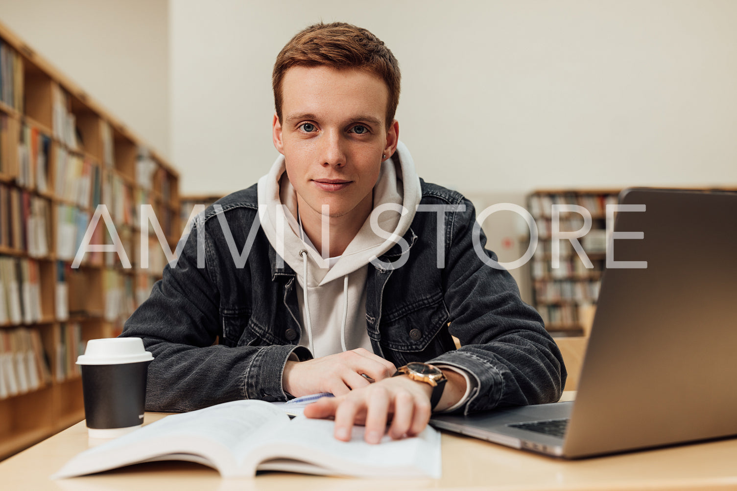 Portrait of a young man sitting at desk in library and looking at camera