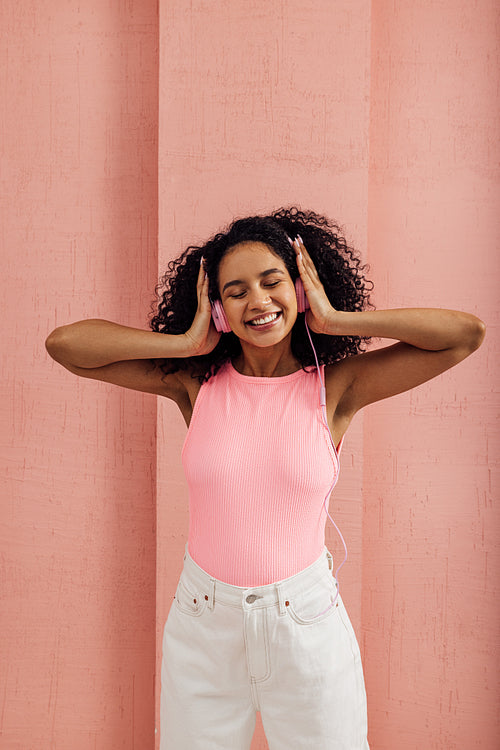 Smiling woman with closed eyes listening to music by pink headph