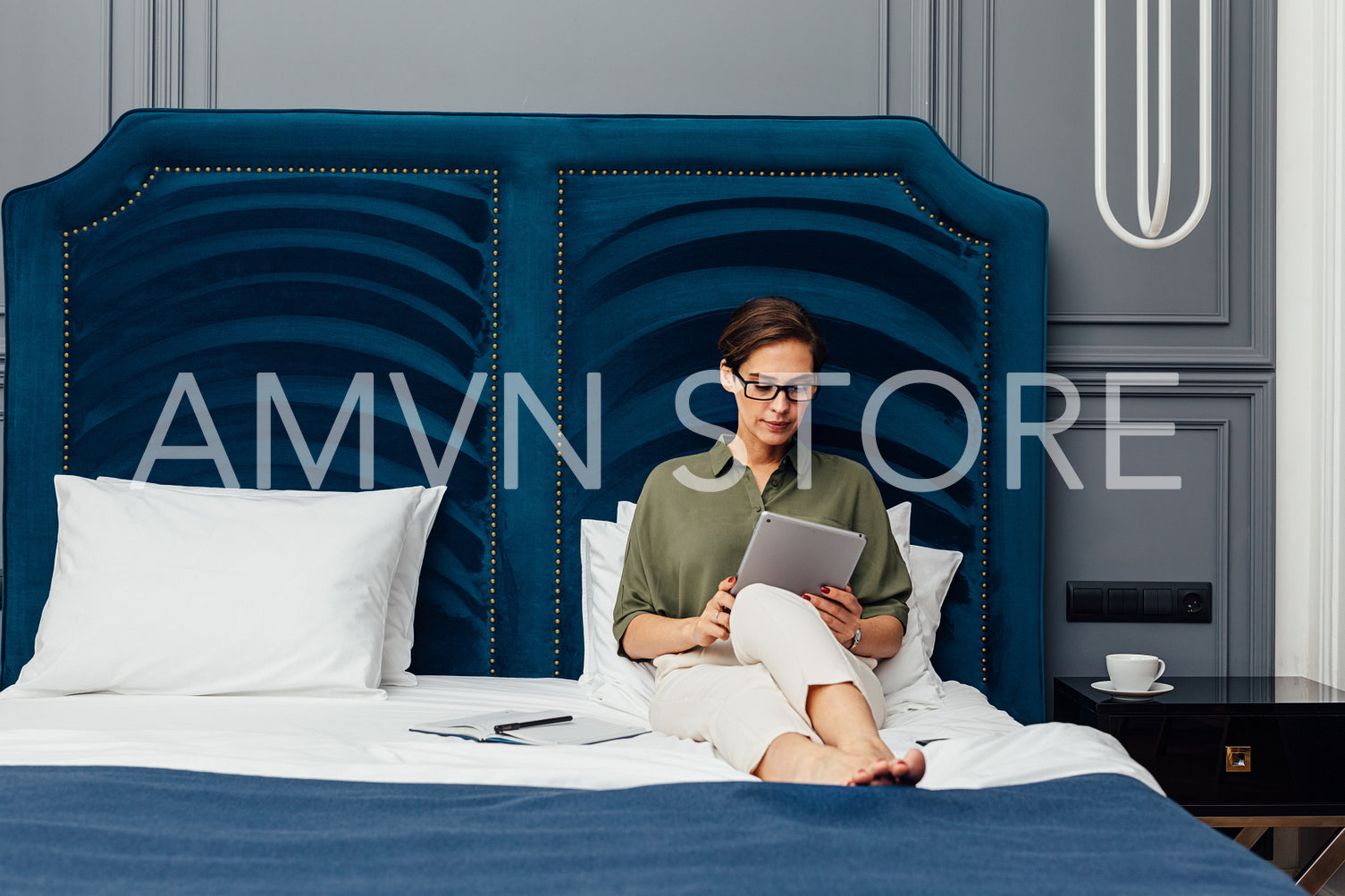 Woman entrepreneur lying on a bed in a luxury hotel room and reading from digital tablet	