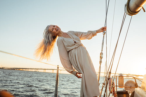 Stylish mature woman holding a rope and enjoying a sunset on a sailboat