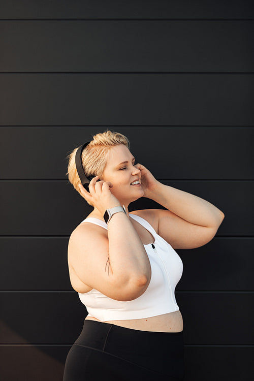 Side view of an oversized woman in sportswear listening to music after training at wall