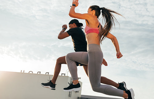 Two athletes jumping in the air during run. Man and woman sprinting together on the roof.