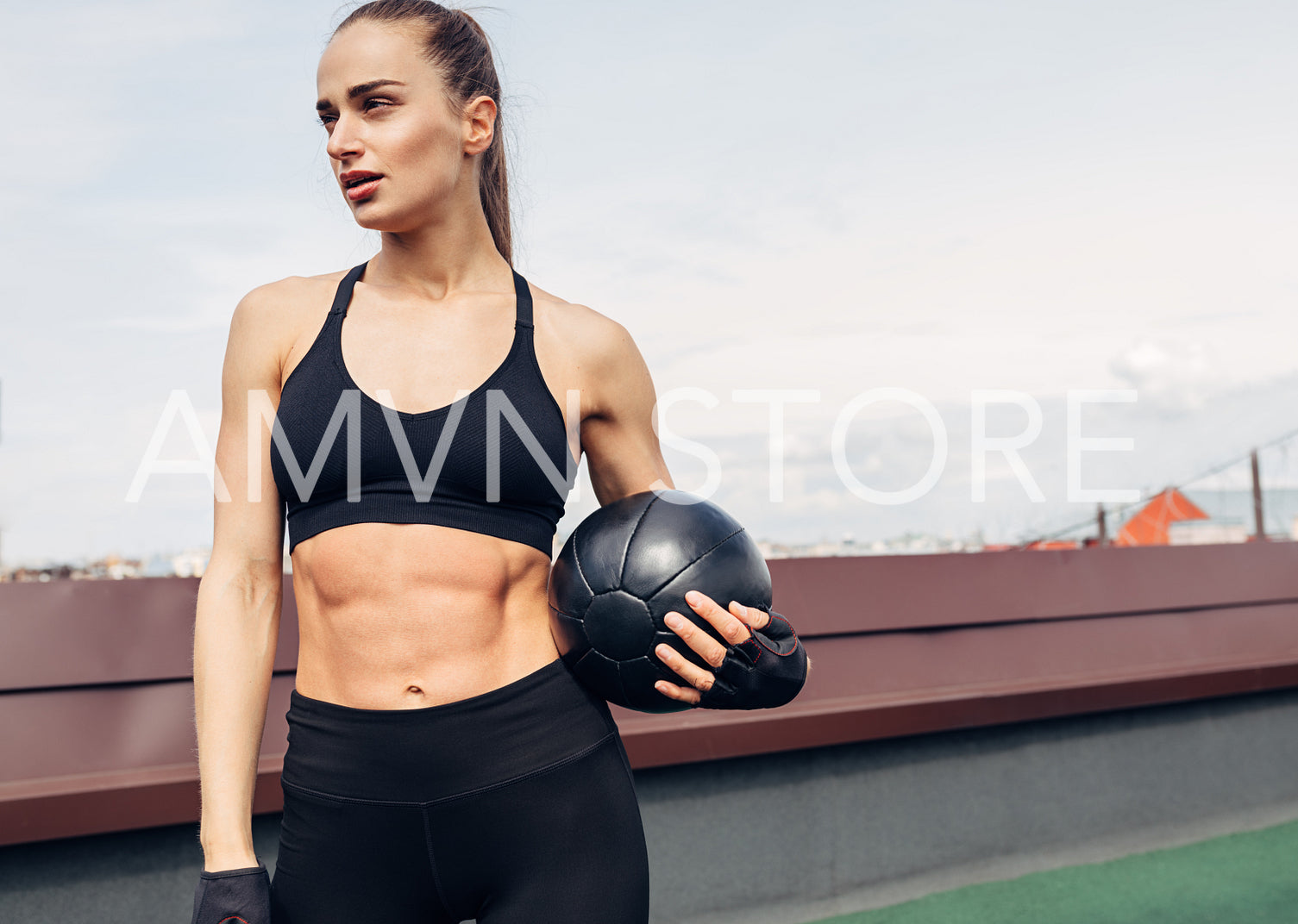 Woman in fitness wear standing outdoors on a terrace with a medicine ball. Young female resting after workout.	
