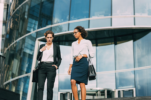 Two colleagues walking down the steps and talking near an office building