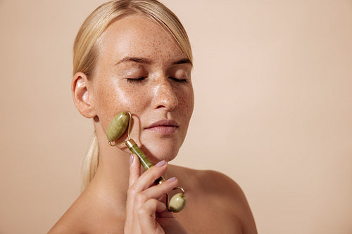 Side view of a young female with freckles massaging face with quartz roller