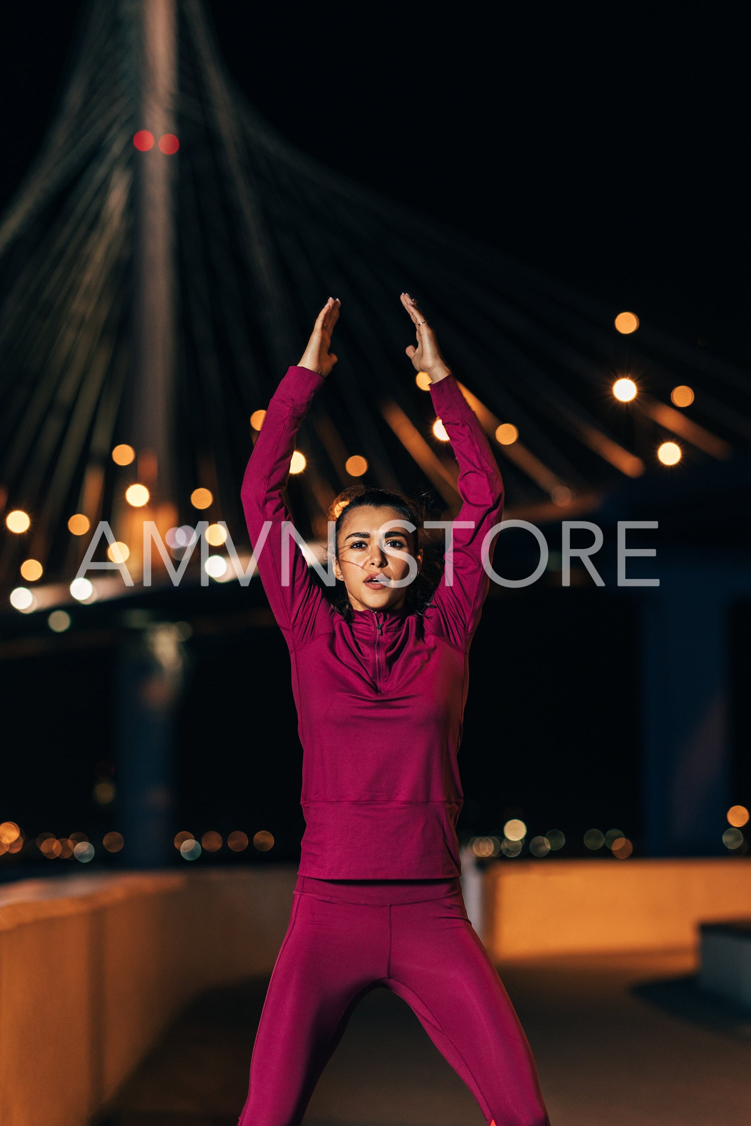 Female athlete in front of bridge at night. Woman wearing sportswear warming up body in the city in the evening.