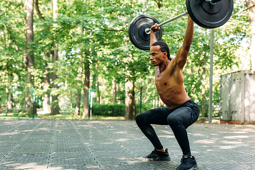 Young athlete performing deadlift exercise with weight bar outdoors