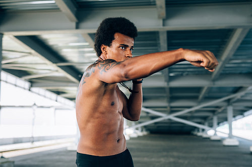 Male boxer practicing her punches under a bridge, doing shadow boxing