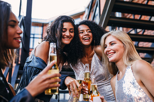 Young people standing with beer bottles on the staircase in the city. Four young women having fun together.