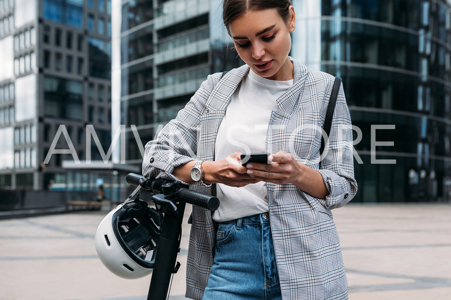 Young woman in stylish clothes holding smartphone while standing in front of an office building 