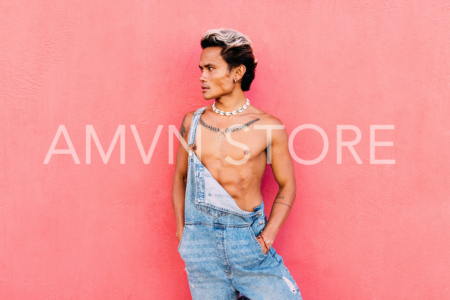 Portrait of a young handsome guy wearing overalls standing outdoors at pink wall