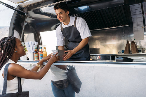 Smiling salesman giving takeaway packaged food to a female customer. Woman taking food from a food truck owner.