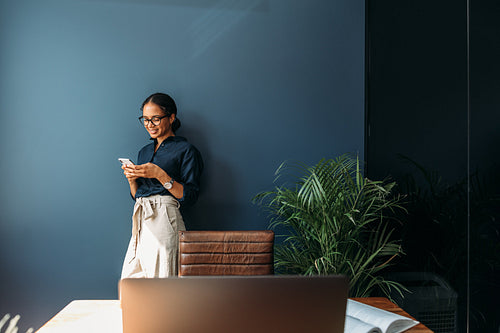 Young woman using a cell phone at a home office. Side view of a female entrepreneur working remotely.