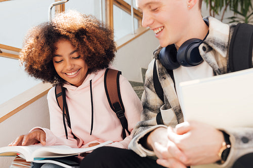 Two classmates are sitting on a stairs and reading. Boy and girl in casuals taking a break after class.