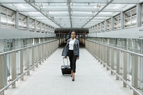 Woman traveller pulling suitcase in airport corridor, front view