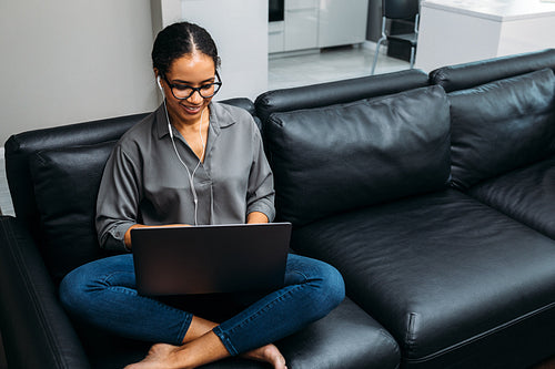 Smiling woman wearing earphones and working on laptop