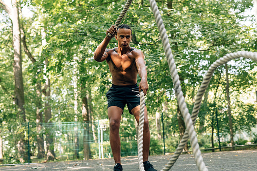 Man doing fitness workout with battling rope on sports ground