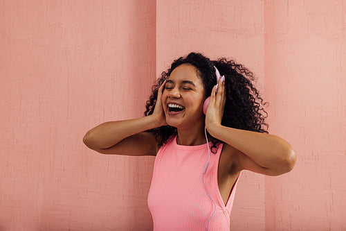 Young woman having fun while listening to music with closed eyes against a pink wall