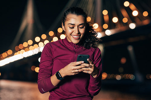 Young female in sportswear typing on smartphone while sitting at night outdoors