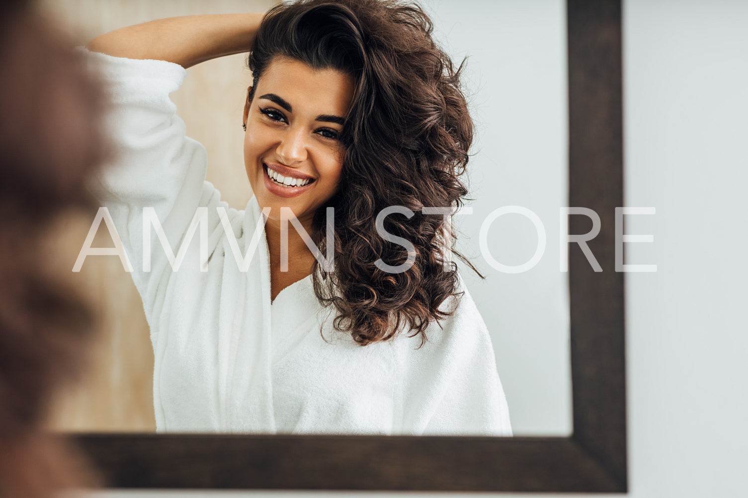 Beautiful smiling woman wearing a bathrobe and holding her hair while standing in front of a mirror	