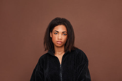 Beautiful young woman with black hair looking at the camera against a brown background