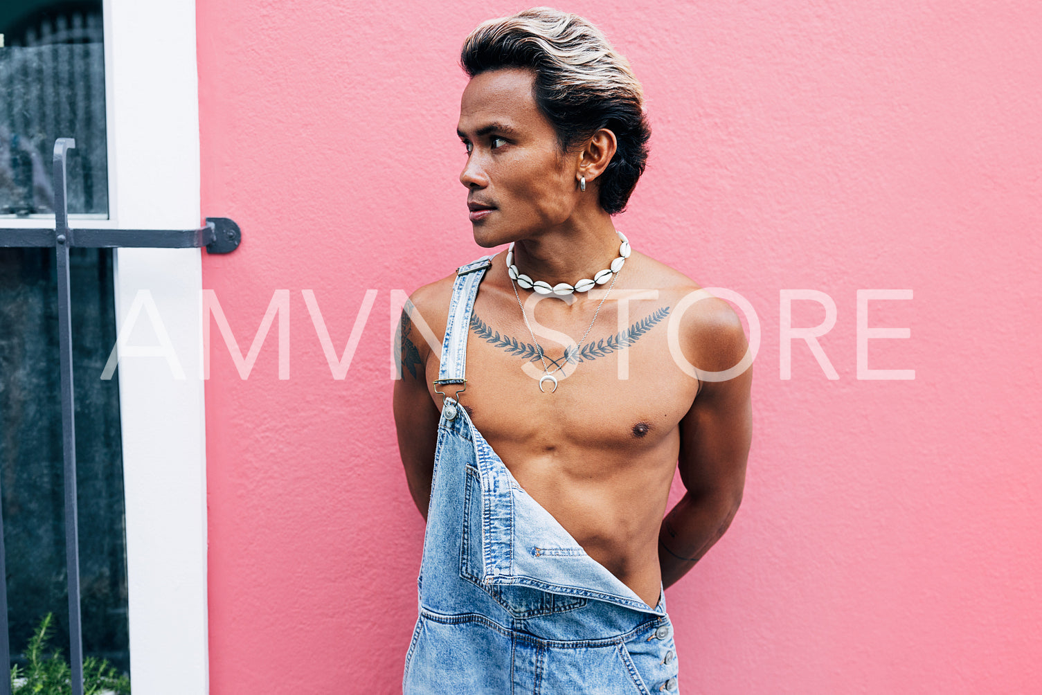 Young stylish man standing outdoors near a house with pink wall and looking away