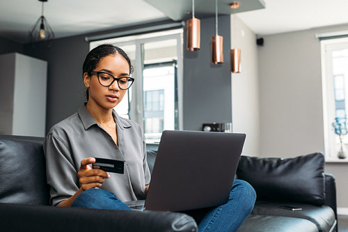 Woman with credit card using laptop in living room. Young female paying online.