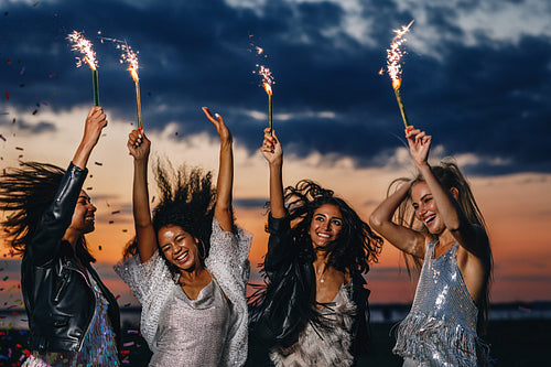 Four happy female friends with sparklers. Stylish women dancing at sunset.