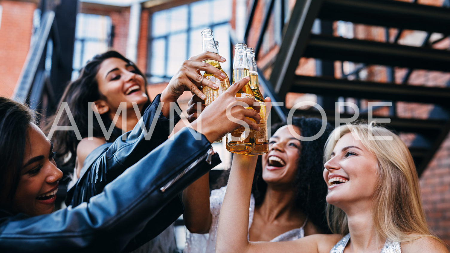 Group of female friends toasting with beer bottles outdoors	