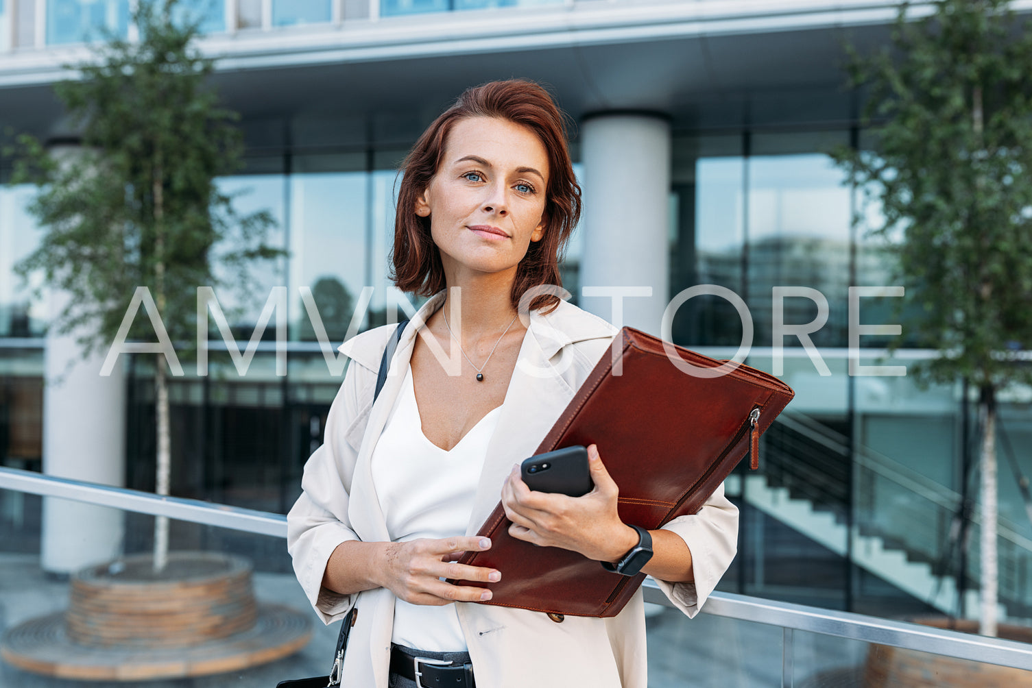 Portrait of a confident middle-aged businesswoman with a leather folder standing against an office building