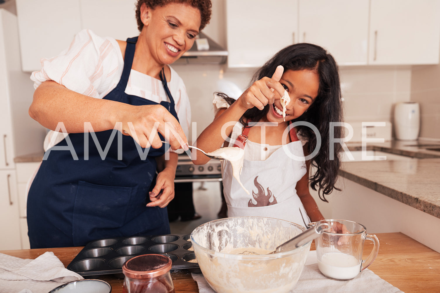 Grandma scoops batter from a bowl with a spoon while granddaughter tests it with her finger