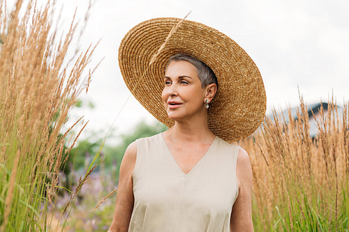 Woman in big straw hat looking away while standing on the field at day