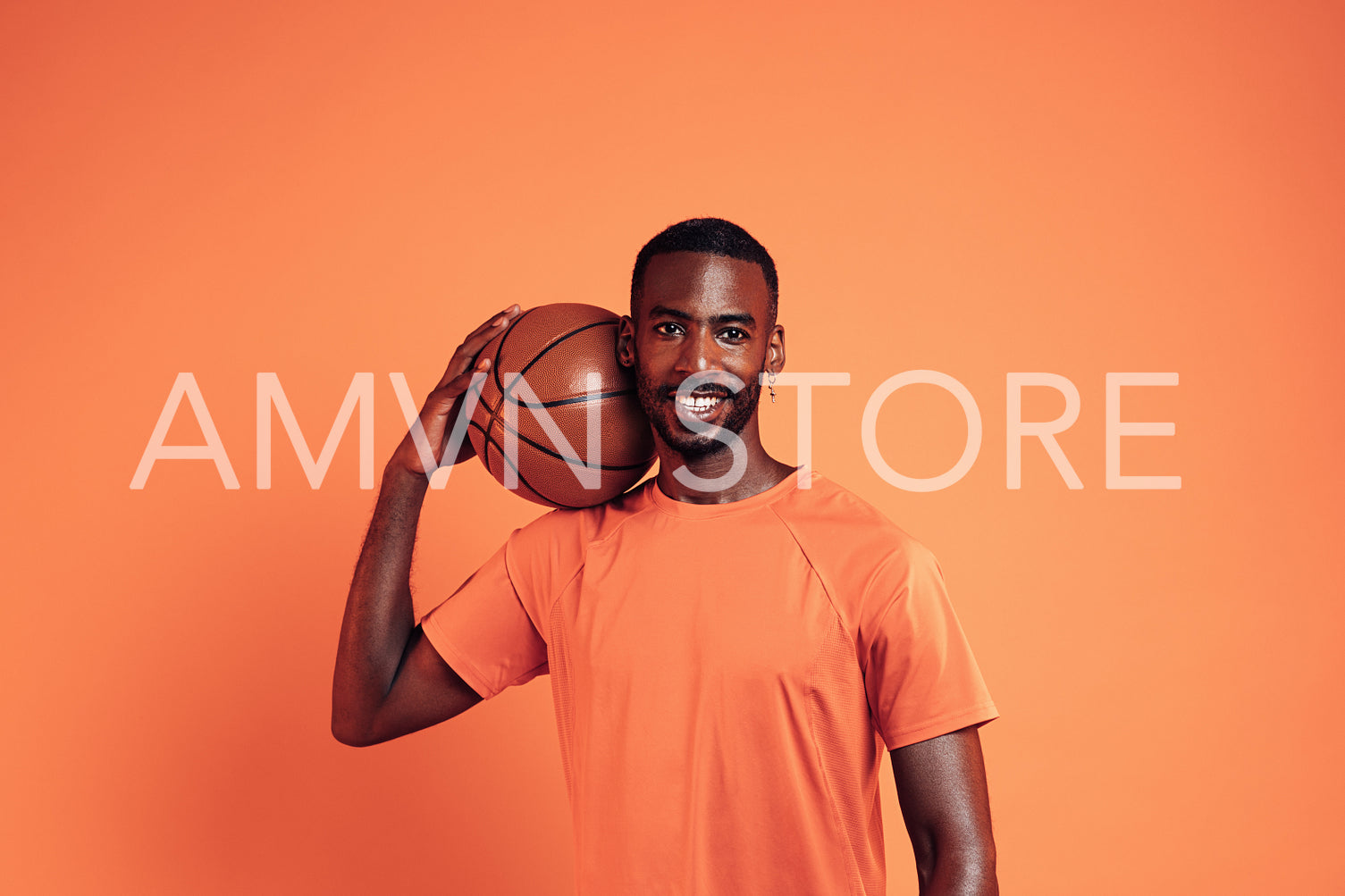 Smiling sportsman with basket ball on his shoulder posing over orange background in studio