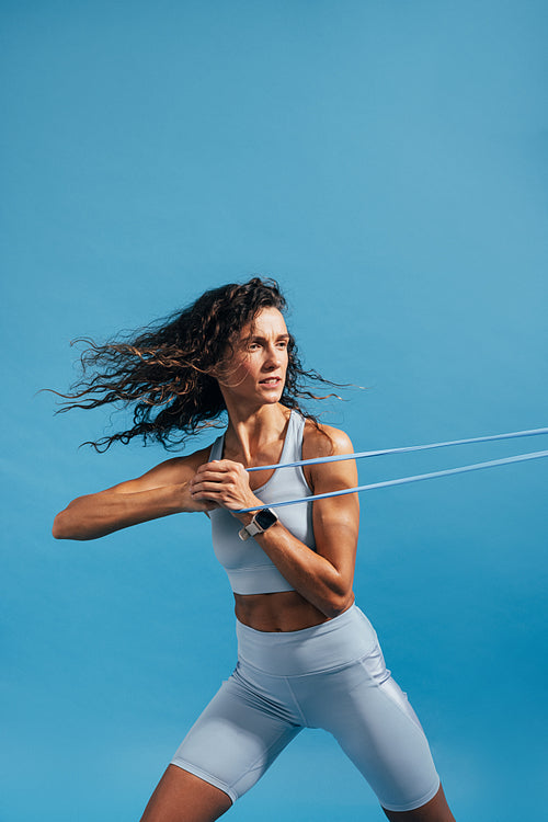 Muscular woman exercising against blue background using resistance bands. Fitness female doing strength workout.