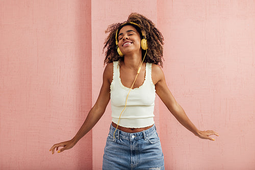 Happy woman enjoying music while standing at pink wall with clos