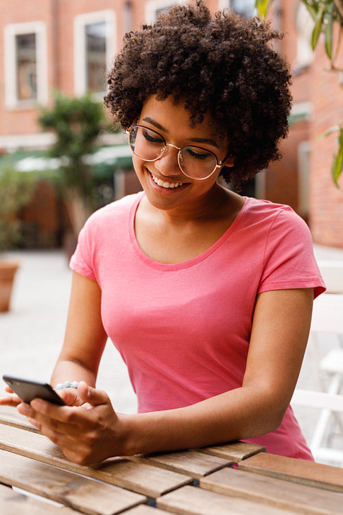 Woman using mobile phone, sitting at table in outdoor cafe