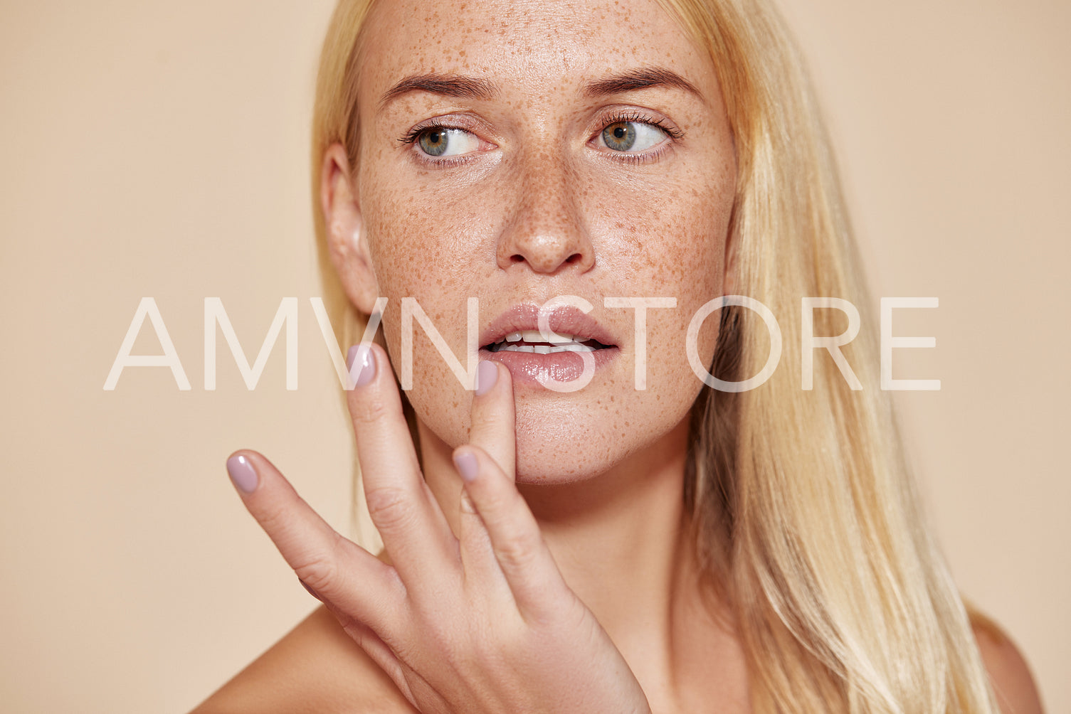 Woman with freckles touching her lip with a finger. Blond female with perfect skin applying balm on her lips.