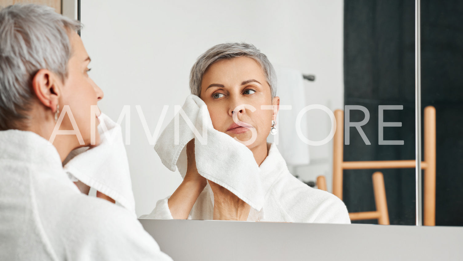 Beautiful mature woman doing morning routine in bathroom wiping the face	