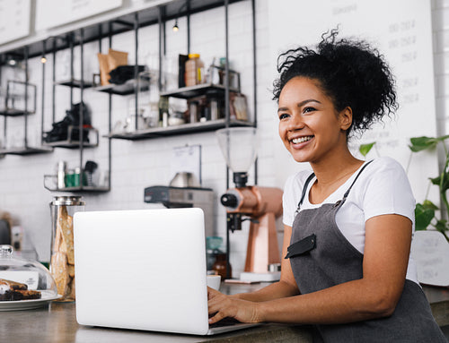 Woman in an apron using a laptop in a coffee shop