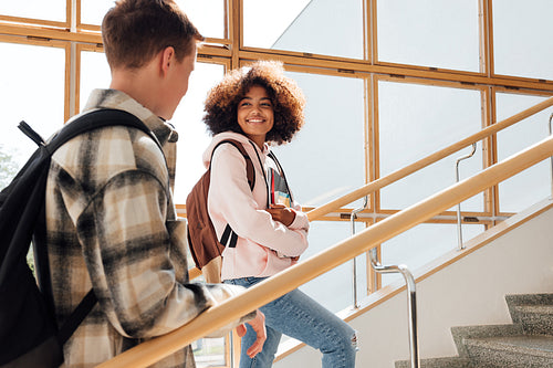 Two classmates climbing college stairs. Smiling woman student looking at her classmate on staircase.