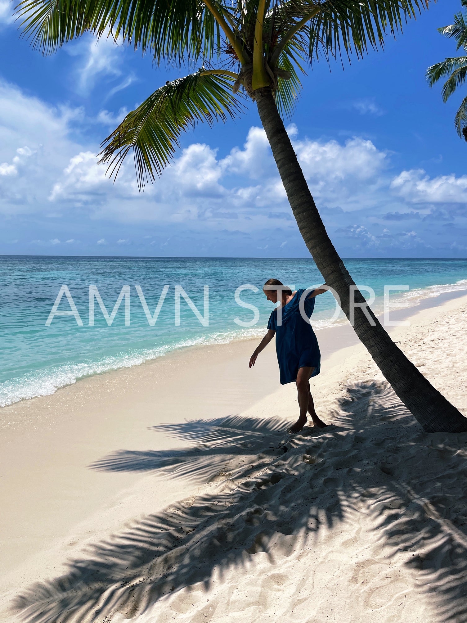 Young woman in blue dress holding a palm tree while standing on tropical island