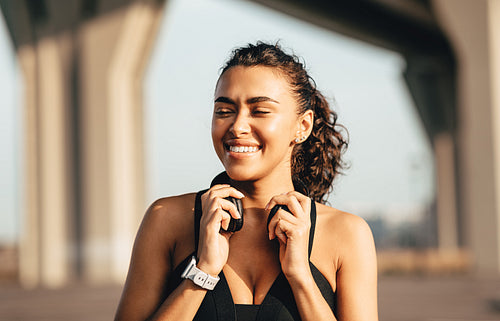 Happy woman relaxing after training standing outdoors and holding headphones