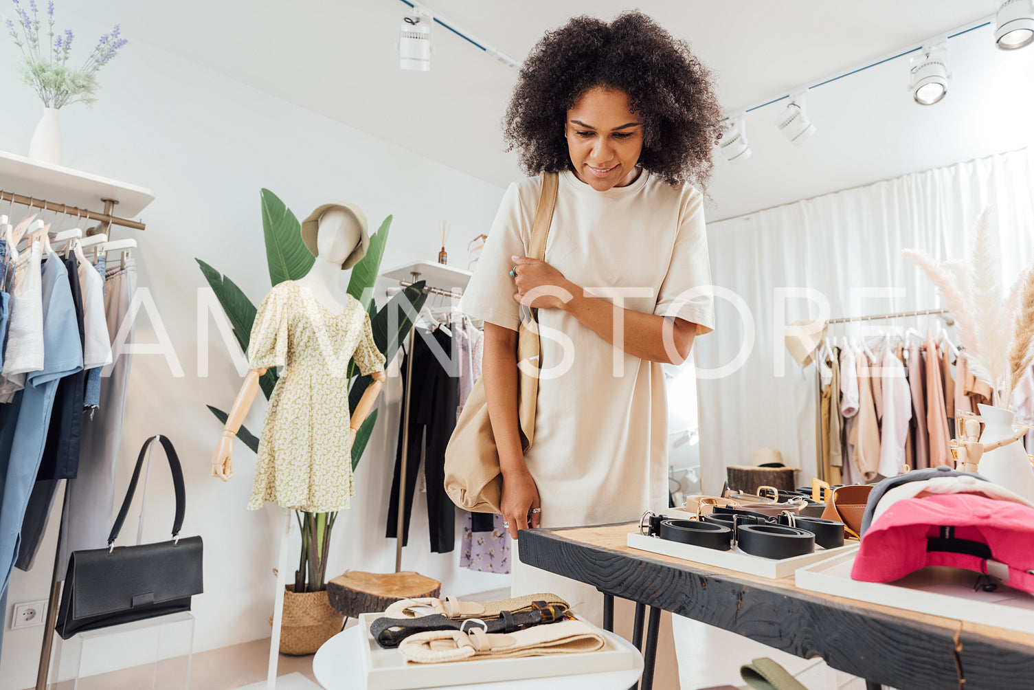 Young woman in stylish clothes standing at a table with accessories in a clothing shop